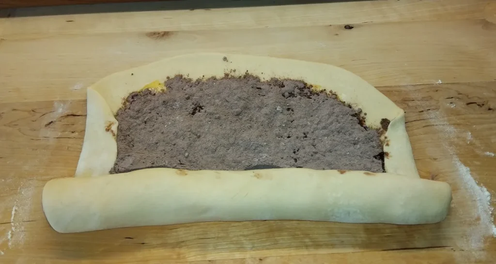 Felhajtott szélű, kakaós töltelékkel megszórt tészta feltekerés közben